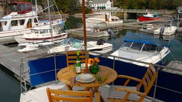 A boat docked at a marina with a table set for two, surrounded by chairs, and a small umbrella.