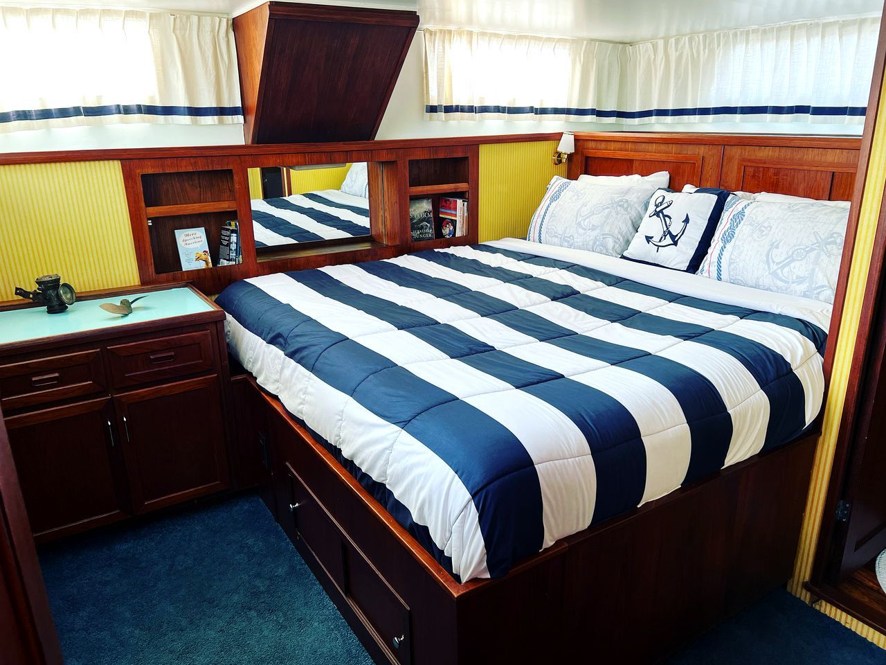 A bed with a striped bedspread, a bedside table with a lamp, and a window with curtains.