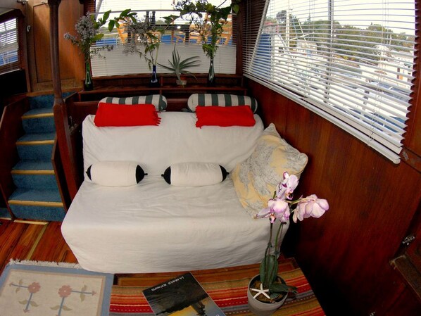 A cozy cabin interior with a sofa, pillows, a vase with flowers, a book, and a window with blinds.