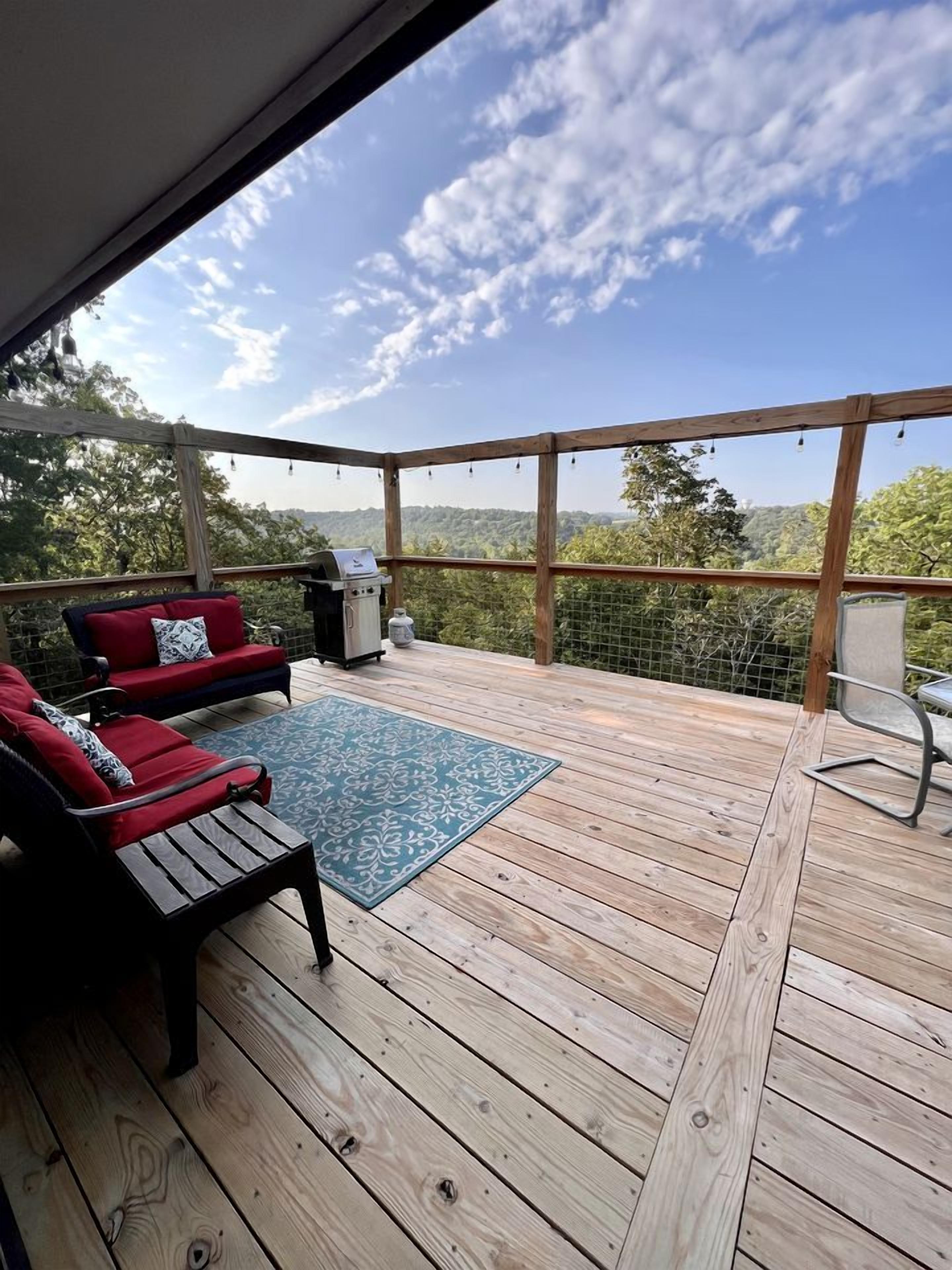 Une terrasse en bois, dotée de mobilier d’extérieur, d’un barbecue et offrant une vue sur le paysage.