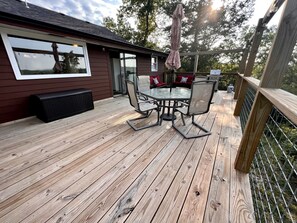 Eine Holzdielen-Terrasse mit Tisch und Stühlen, einem überdachten Sonnenschirm und einem Haus im Hintergrund.