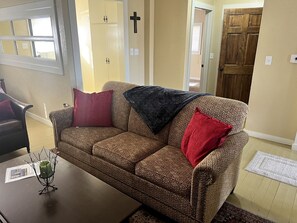 A living room with a patterned sofa, a coffee table, and a cross on the wall. - Cozy Cabin Rental near Table Rock Lake in the Ozark Mountains, Missouri (Hollister)