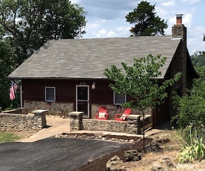 A rustic cabin with a stone foundation, a chimney, and a small porch with red Adirondack chairs. - Cozy Cabin Rental near Table Rock Lake in the Ozark Mountains, Missouri (Hollister)