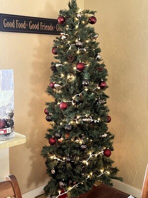 A Christmas tree with lights and ornaments, a sign above it, and a clear glass object on a table. - Cozy Cabin Rental near Table Rock Lake in the Ozark Mountains, Missouri (Hollister)