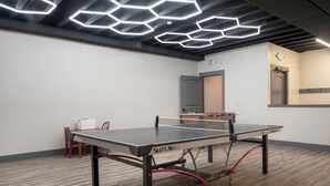 A ping pong table in a room with a hexagonal ceiling light fixture, an exit sign, and a door in the background. - NEW Beautiful 2-bedroom condo in Granby perfect for your getaway (Granby)