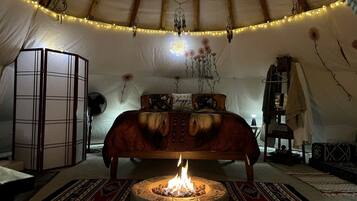 A cozy interior with a bed, a central fire pit, and string lights.