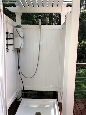 A white wooden outdoor shower enclosure with a hose and a control box.