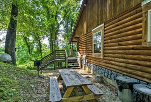 A wooden cabin with a wooden deck, a picnic table, and a trash can.