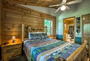 A wooden cabin bedroom with a bed, nightstands, a ceiling fan, and a window.