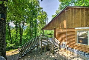Eine Holzhütte mit Stein Fundament, einer Holztreppe, die zu einer Veranda führt, und Blick auf einen bewaldeten Bereich.
