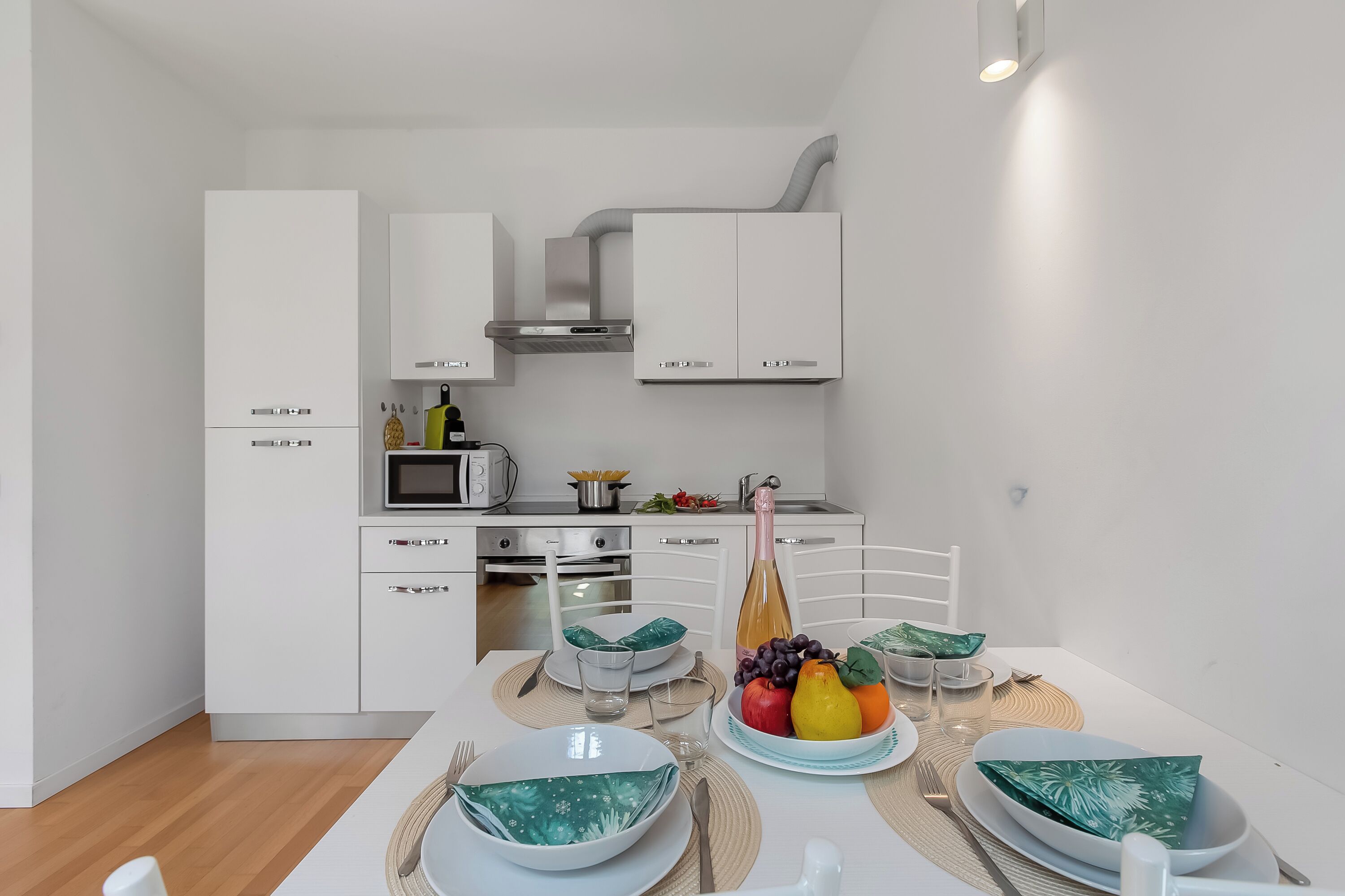 A modern kitchen with white cabinetry, a microwave, and a dining area with a table set for two.