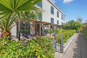 A modern building with a patio area, outdoor seating, and lush greenery. - Mediterranea Apartments (Savona)