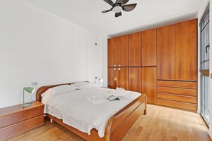 Un dormitorio con cama, armario de madera, mesita de noche, lámpara y ventilador de techo.