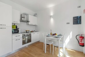 A modern kitchen with white cabinets, a built-in oven, and a dining area with a white table and chairs. - Mediterranea Apartments (Savona)
