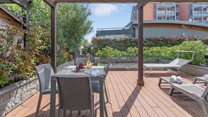 A covered outdoor area with a table and chairs, a lounge chair, and a pool. - Mediterranea Apartments (Savona)