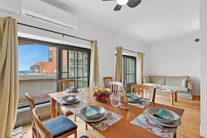 Ein Essbereich mit Tisch für vier Personen, einer Couch und einem Balkon mit Blick auf Gebäude.