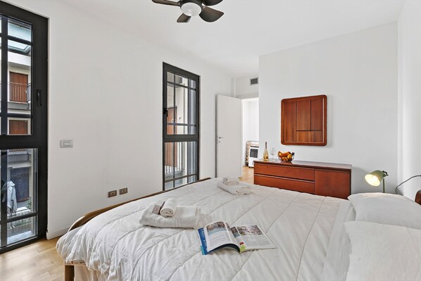 Un dormitorio con una cama, una mesita de noche con lámpara, un aparador de madera y una ventana con vistas al exterior.