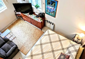 A bedroom with a bed, a chair, a dresser, a TV, a poster, and a radiator.