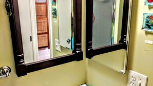 Une salle de bain avec un miroir, un lavabo et une porte donnant sur une autre pièce.