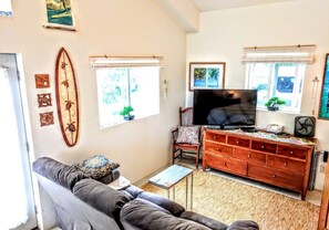 Ein Wohnzimmer mit einer Couch, einem Fernseher, einer Holzkommode und einer Surfbrett-Dekoration.