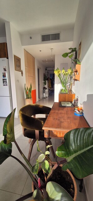 A dining area with a wooden table, a velvet chair, and potted plants. - Bright & Stylish Boho Home w\ Botanical Terrace, by a grove -with a safe Mamad (Tel Aviv-Yafo)