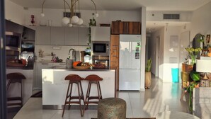 Et moderne køkken med en central ø, barstole, et spisebord og en opholdsstue med sofa og planter.