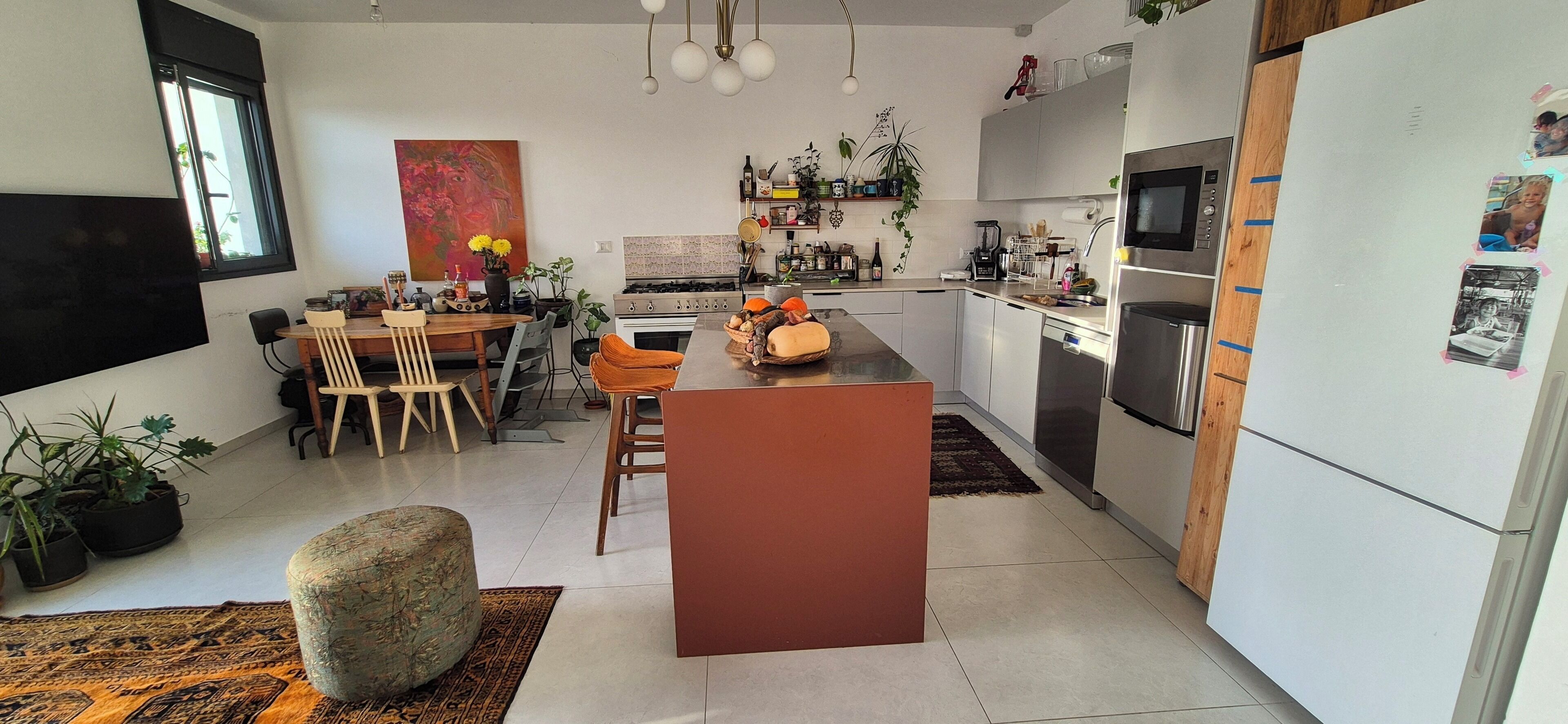 A modern kitchen with a central island, dining area with chairs, and a refrigerator with photos.