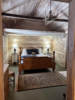 Een slaapkamer met houten lambrisering, een bed, twee nachtkastjes met lampen, een vloerkleed en een kroonluchter.