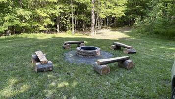 A circular fire pit surrounded by logs in a grassy area with trees in the background.