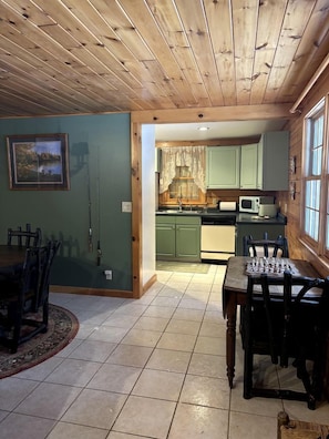 Un comedor con mesa y sillas de madera, una cocina con armarios verdes y vistas a través de una puerta abierta.