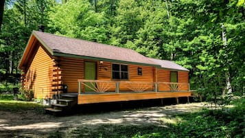 A log cabin with a porch, a chimney, and a small deck.