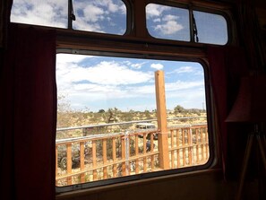 Ein Fenster mit Blick auf eine Wüstenlandschaft, ein Holzzaun und ein Fahrzeug auf einer Straße.