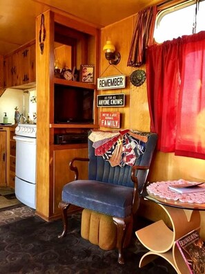 Un espace de vie compact comprenant un coin cuisine, une chaise en bois, une table avec un livre et un rideau rouge.