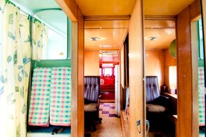 A narrow corridor with two seating areas, a small kitchenette, and a window with curtains. - Superb Elevated Trailer for Unique Vacation in San Bernardino County, California (Joshua Tree)