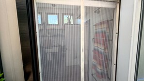A sliding glass door with a mesh screen, leading to a room with a tiled floor and a visible window.