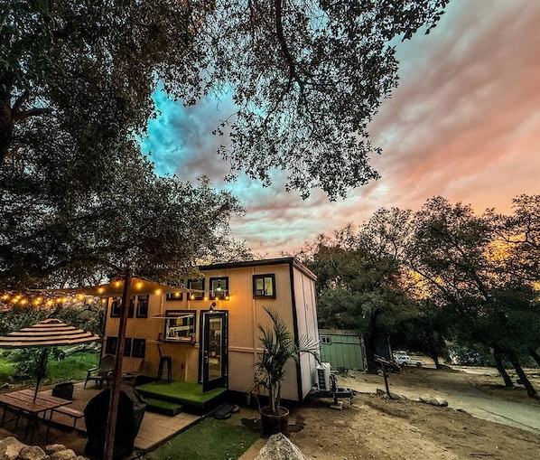 Una casita con césped verde, mobiliario exterior y luces de cuerda.