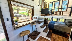 A compact living space with a kitchen area, a dining table, a bed, and a TV.
