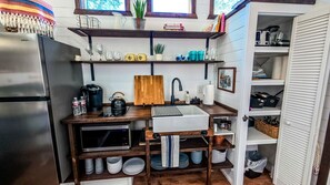 A compact kitchen with a built-in sink, wooden shelves, and a stainless steel refrigerator.