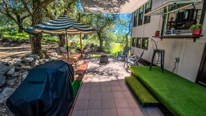 A patio with a barbecue grill, outdoor seating, and a covered area with a striped umbrella.