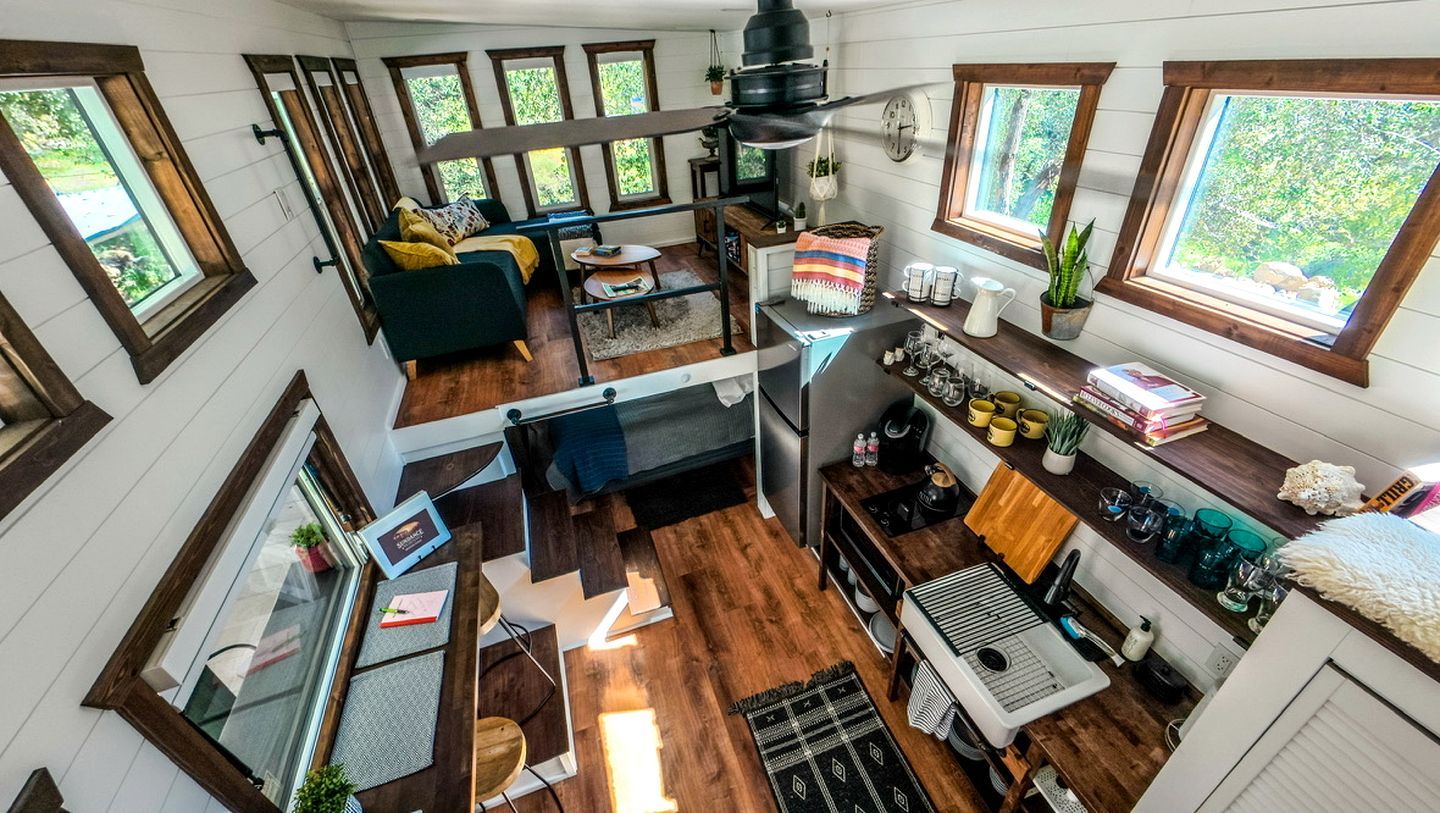 Un espace de vie compact et ouvert, comprenant une cuisine, un coin repas et un coin salon, avec de grandes fenêtres et une zone de couchage en mezzanine.