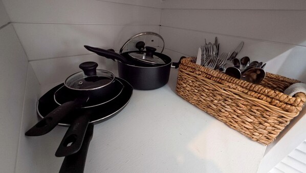 A kitchen with a white countertop, a black frying pan, a pot with a lid, and a woven basket containing utensils.