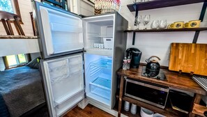 A compact kitchen with a refrigerator, a coffee maker, and a kettle on a wooden countertop.