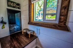 Habitación que admite mascotas con cama para mascotas, dos cuencos sobre un soporte de madera y una ventana con vistas a sombrillas exteriores.