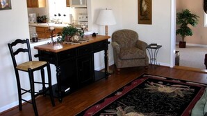 A kitchen with wooden cabinets, a dining table, two chairs, a lamp, and a rug. - Charming Cottage Overlooking Gorgeous Citation Bass and Bream Pond near Charlottesville (Gordonsville)