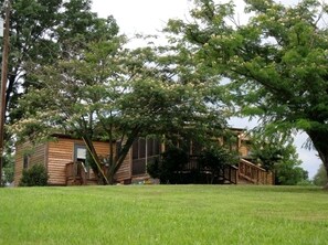 Eine Holzhütte mit Veranda, umgeben von einer grünen Wiese und großen Bäumen.