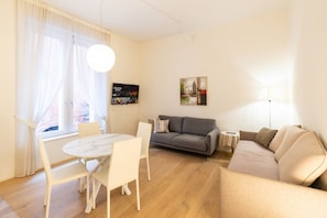 Ein Wohnzimmer mit einer Couch, einem Esstisch mit Stühlen, einem Fernseher und einem Bild an der Wand.