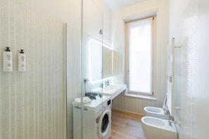 Ein modernes Badezimmer mit Duschkabine aus Glas, einer eingebauten Waschmaschine, einem Waschbecken und einer Toilette.