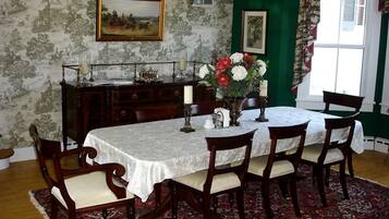 A dining room with a table set for six, surrounded by wooden chairs, a patterned wallpaper, a green accent wall, and a window with curtains.