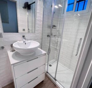 A modern bathroom with a white sink, a mirror, and a glass-enclosed shower. - Luz Suite Seville Downtown 2026 (Seville)