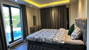 Une chambre moderne avec un grand lit, une petite table de chevet, une chaise, une vue sur l’extérieur et un plafond doté d’un éclairage encastré.